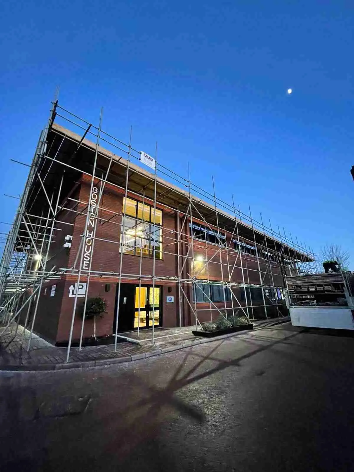 Designed scaffold erected to a bespoke configuration around a commercial office building at dusk